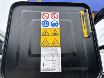 Mack GR64F crane cab door showing warning labels and a chart, with safety pictograms and a yellow ruler on the edge.