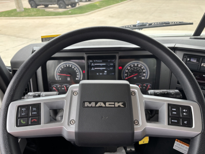 Mack GR64F truck dashboard steering wheel with Mack logo, gauges, and control panels; front view from cockpit showing instrument cluster and steering wheel.