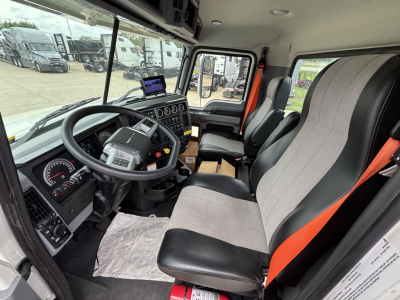Interior of a Mack GR64F truck cab showing steering wheel, dashboard, and two-tone seats with orange seat belts.