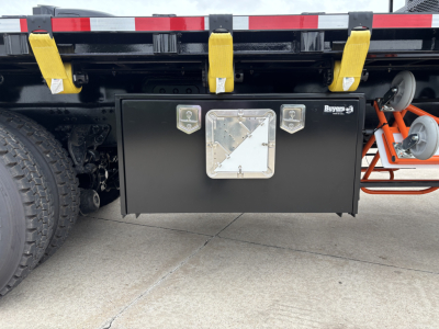 Mack GR64F truck rear view showing a large black rectangular toolbox under the chassis with metal handles and a central diamond-shaped access panel.