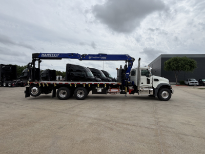 Truck-mounted crane on a Mack GR64F chassis showing blue Manitex boom labeled with branding and multiple axles with a white cab.