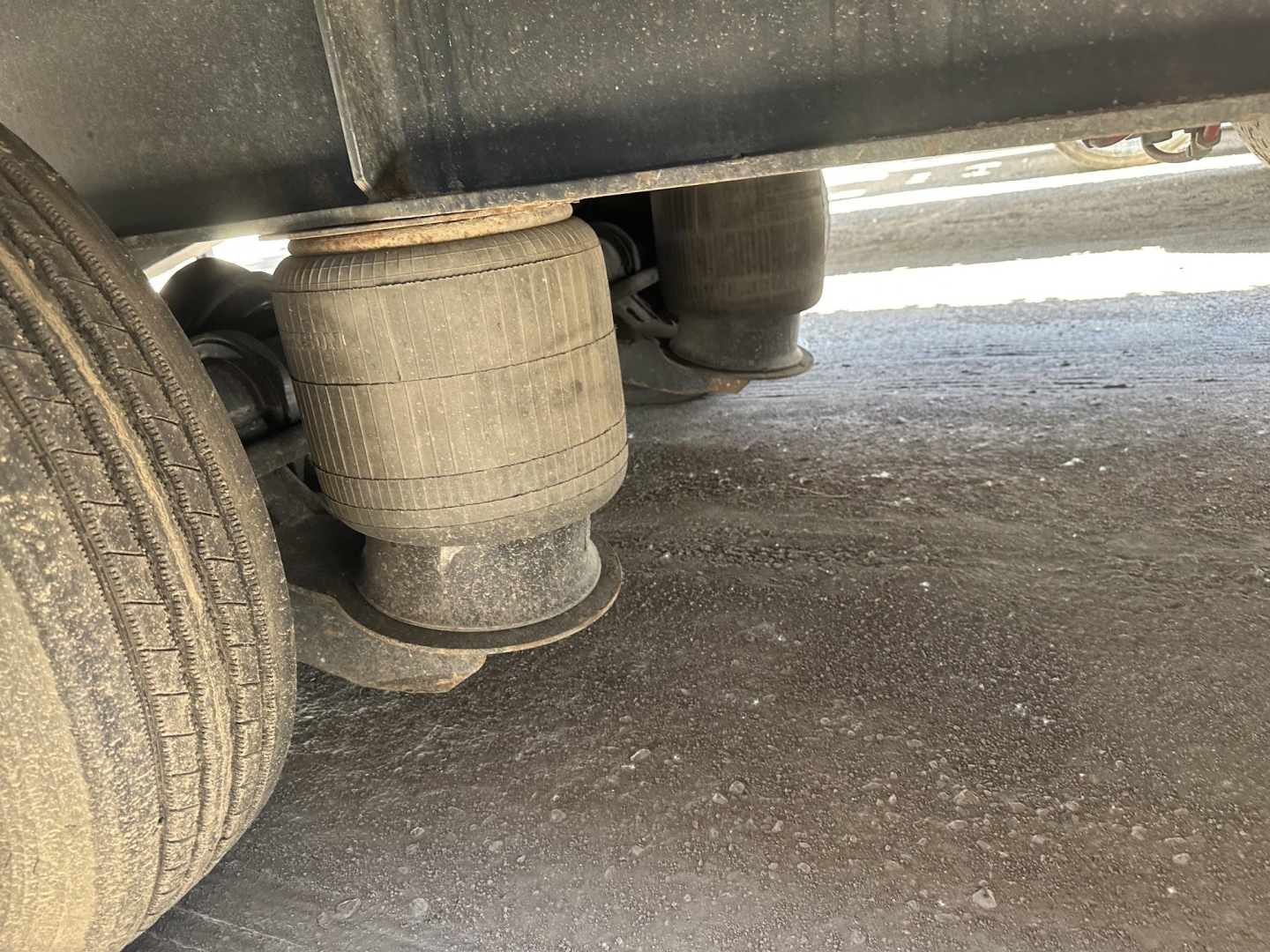 Rear view of a Great Dane drop deck trailer with two large air bags/air suspension units under the deck and a wheel nearby.