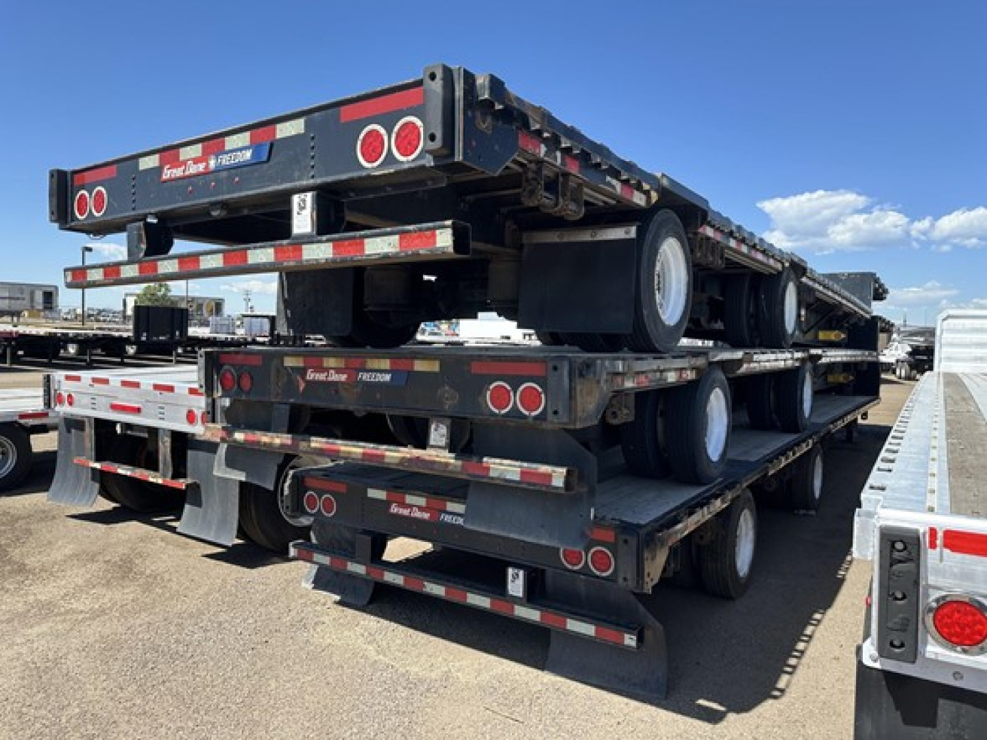 Great Dane steel spread air drop deck trailer stack showing multiple flatbed trailers with dual rear wheels and red/white safety markings.