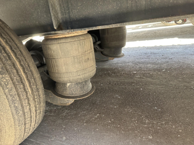 Rear view of a Great Dane drop deck trailer with two large air bags/air suspension units under the deck and a wheel nearby.