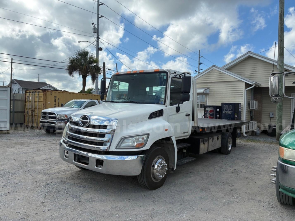 2013 Hino conventional cab tow truck with flatbed, front grille chrome, white body, side mirrors, and a blue sky with clouds.