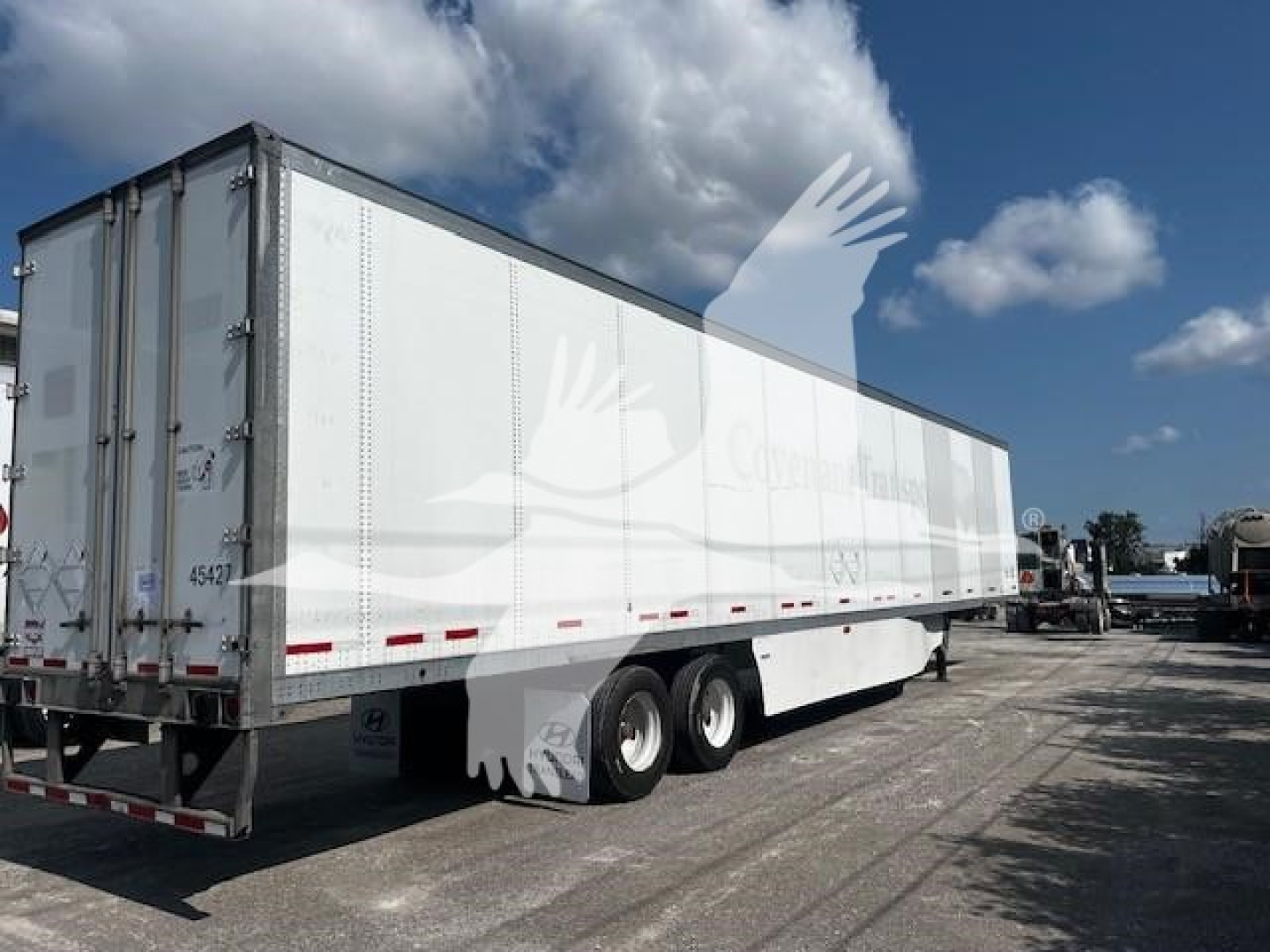 Trailer side view showing a white Wabash dry van trailer with tandem axles and rear doors.