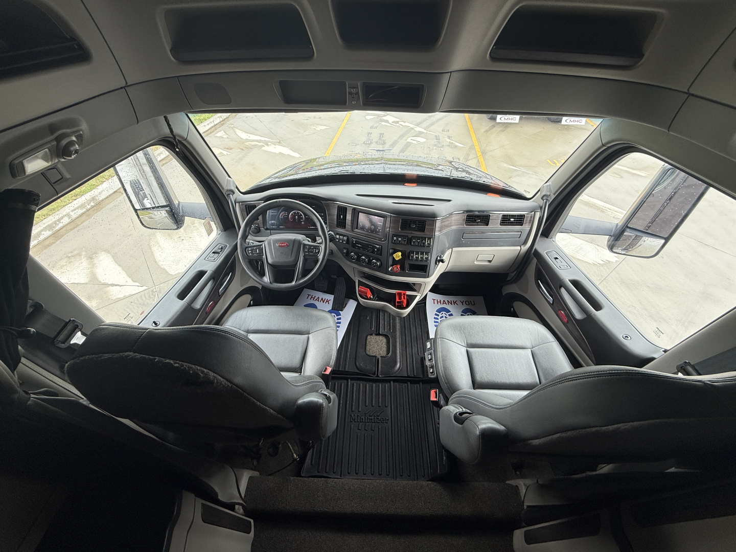 Truck interior cab view of a 2024 Peterbilt 579, capturing the dashboard, steering wheel, and two front seats from behind the passenger area.