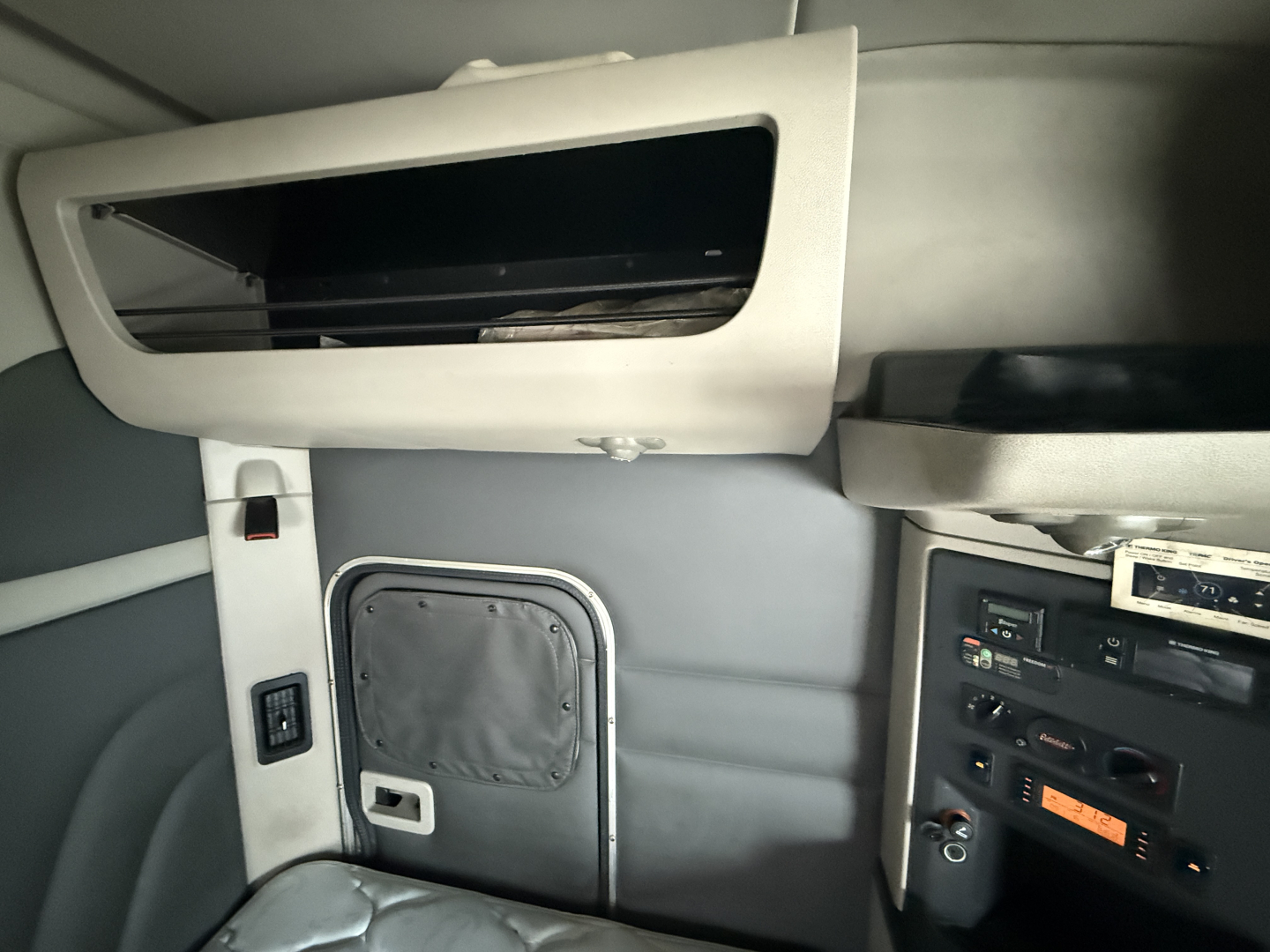 Truck cab interior showing upper storage shelf and side panel with small door, control switches, and dashboard components.