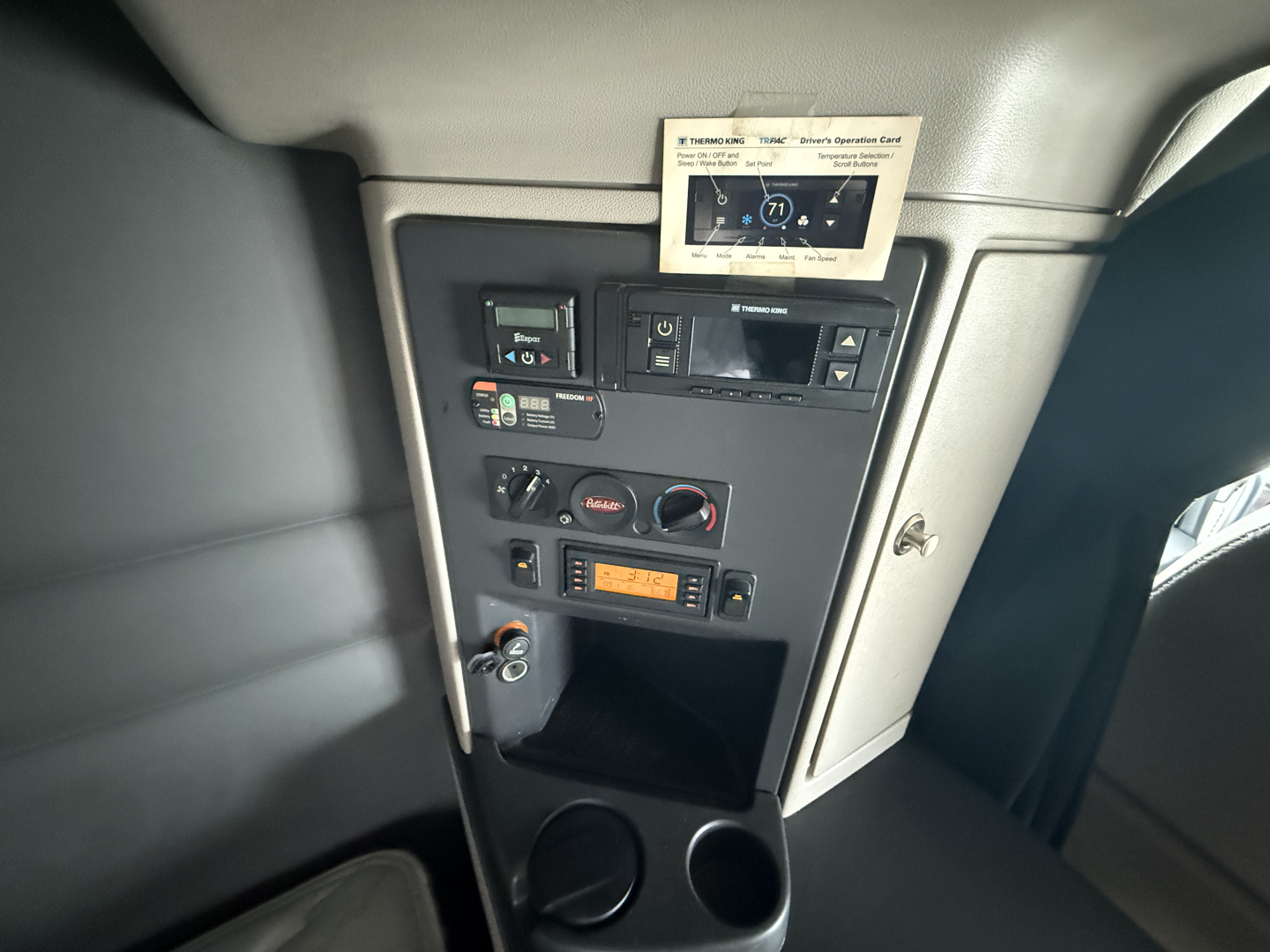 Peterbilt cabin console showing control panel with switches, cup holders, and small display screen.