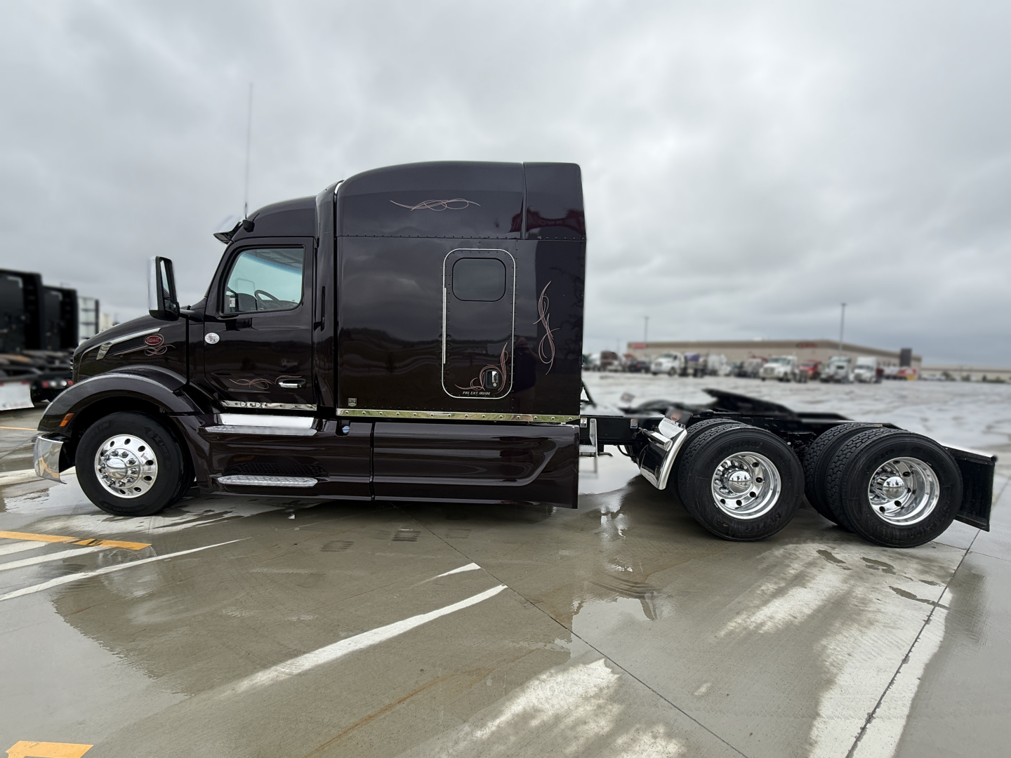 Peterbilt 579 conventional sleeper tractor seen in side profile with dark brown/black paint, two-axle rear, chrome wheels, and side steps. VIN plate and stock number not visible in image.