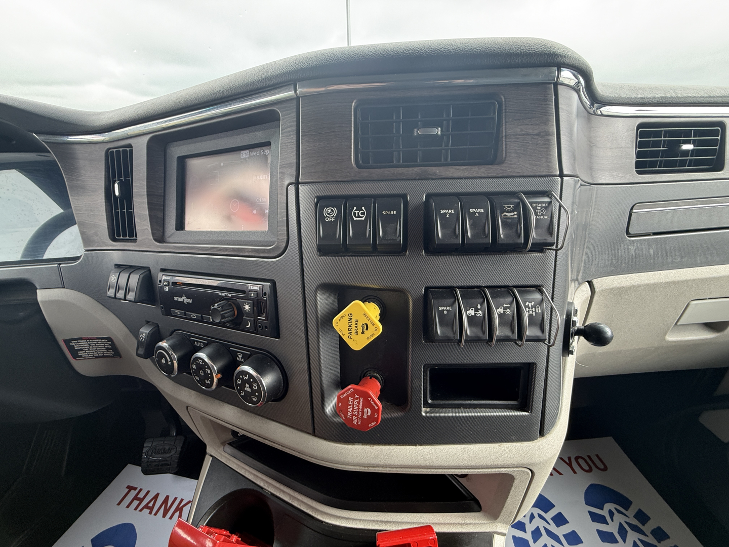 Peterbilt 579 dashboard view showing control switches, gauge cluster, climate controls, and yellow and red knobs in the center console.