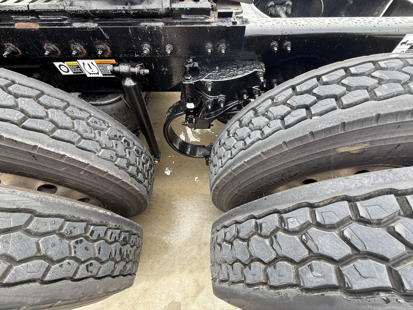 Truck chassis area showing dual rear axles with tires, undercarriage components and suspension in view.