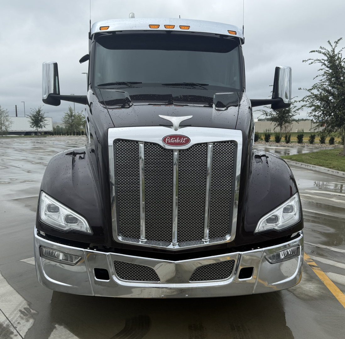 Peterbilt 579 front view showing chrome grille and headlights with Peterbilt emblem, black body, wet pavement reflection.