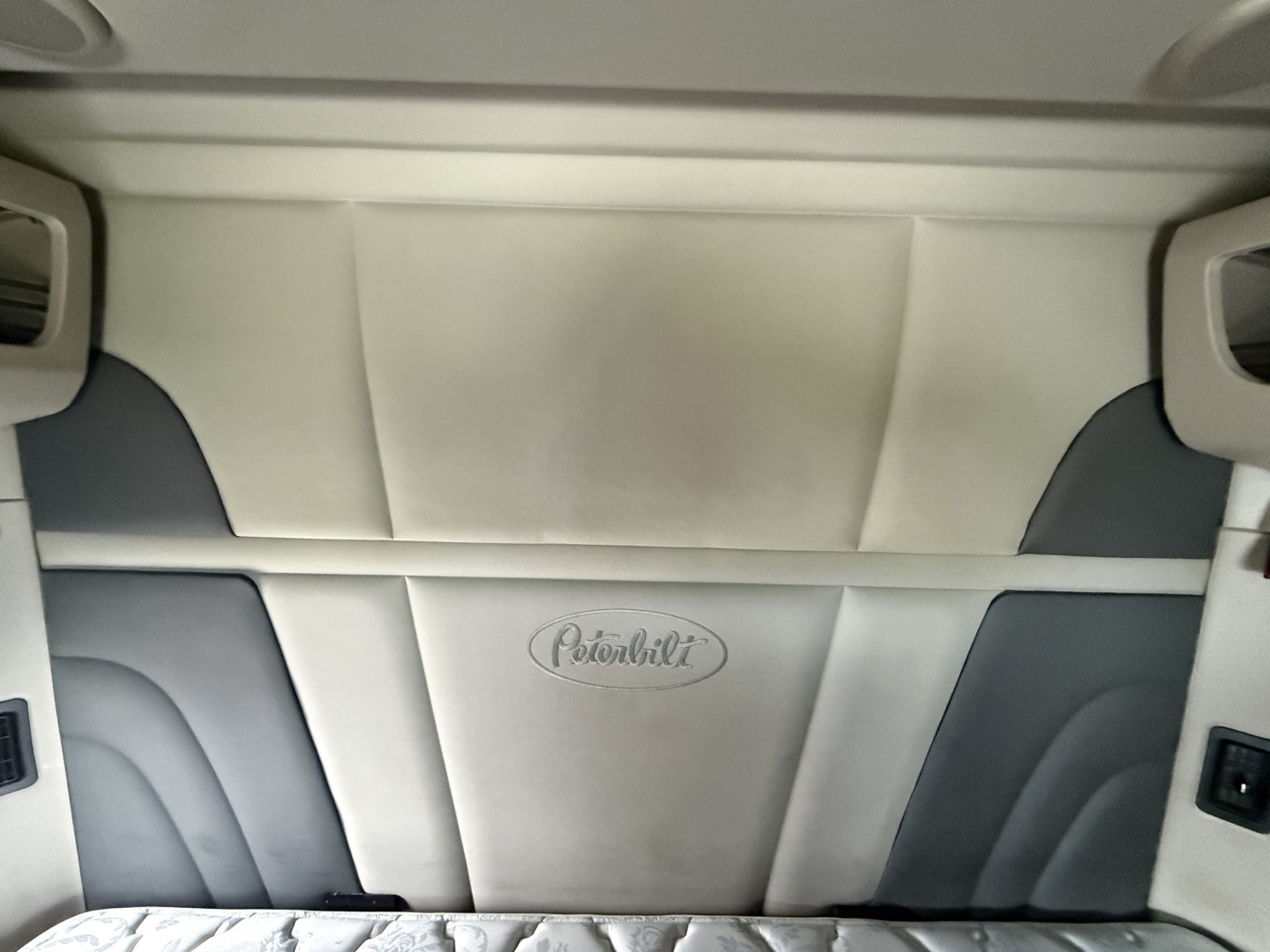 Peterbilt interior headliner and sleeper cab seating area with Peterbilt logo on light-colored upholstery.