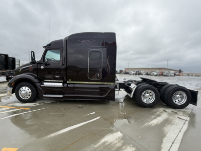 Peterbilt 579 conventional sleeper tractor seen in side profile with dark brown/black paint, two-axle rear, chrome wheels, and side steps. VIN plate and stock number not visible in image.