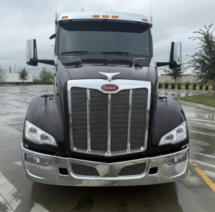 Peterbilt 579 front view showing chrome grille and headlights with Peterbilt emblem, black body, wet pavement reflection.