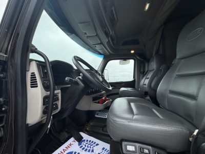 Peterbilt 579 cab interior showing steering wheel, dashboard, driver seat, and passenger seat with grey leather. Window and door area visible.