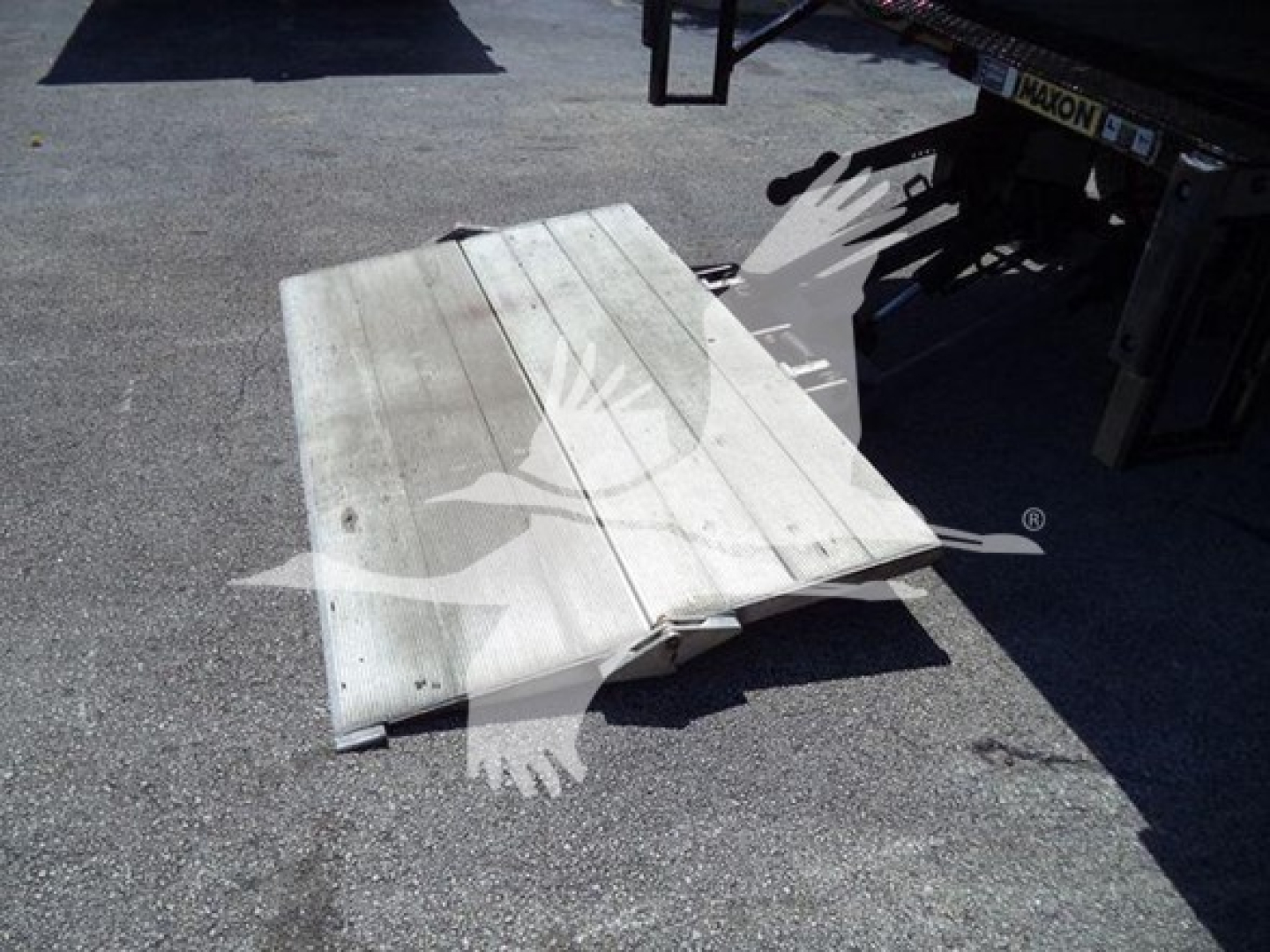 Flat metal loading ramp or step attached to a truck trailer seen on asphalt.
