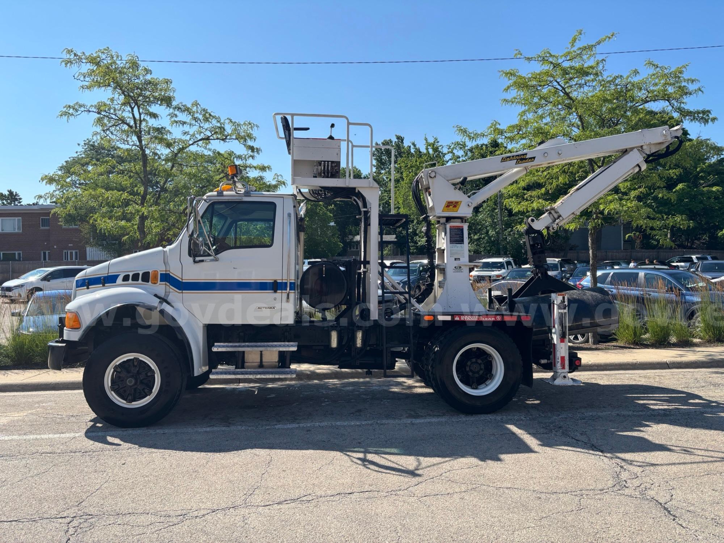 Grapple truck side view showing elevated platform, crane arm, and hydraulic hooks with white cab and blue stripe