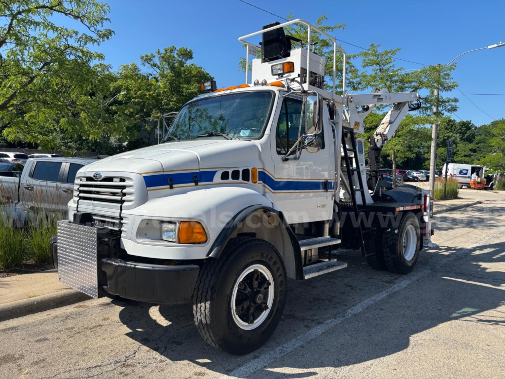 White Sterling truck with a heavy-duty crane/boom and platform on the back, towing-ready utility vehicle with ladder rack, headlights, and warning lights.