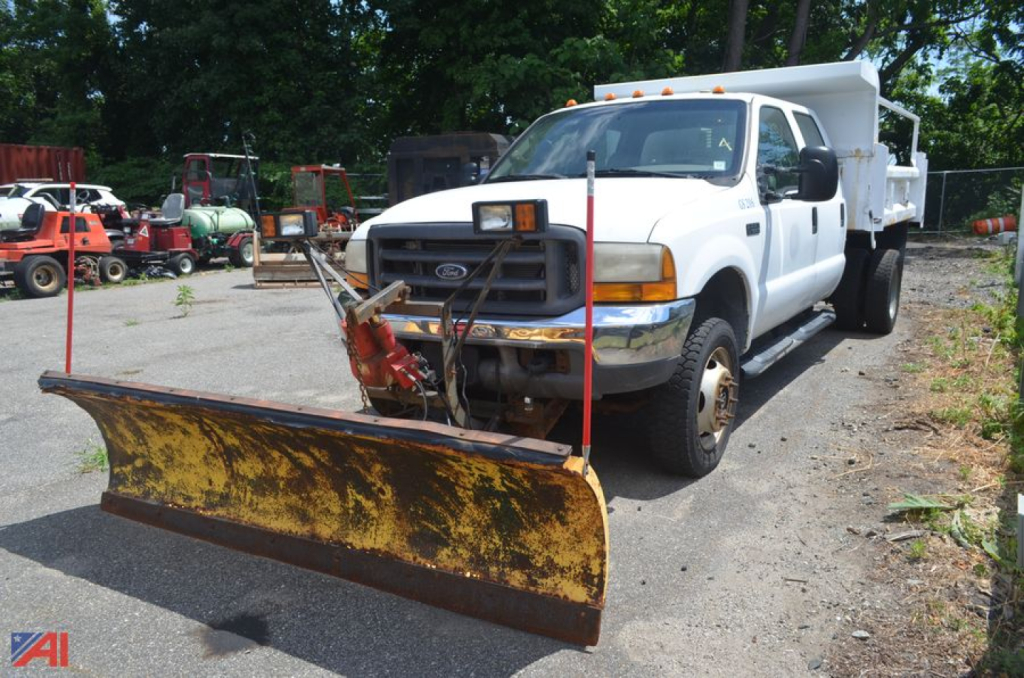 Ford F-550 Super Duty dump truck with a yellow front plow blade attached, white cab, and dump bed in background.