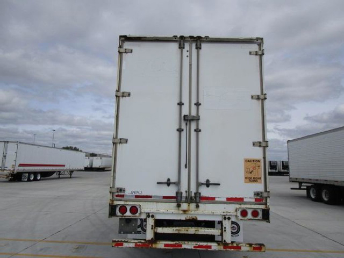 Stoughton van rear showing double cargo doors with hinges, taillights, and safety decals; stock on lot with other trailers in background.