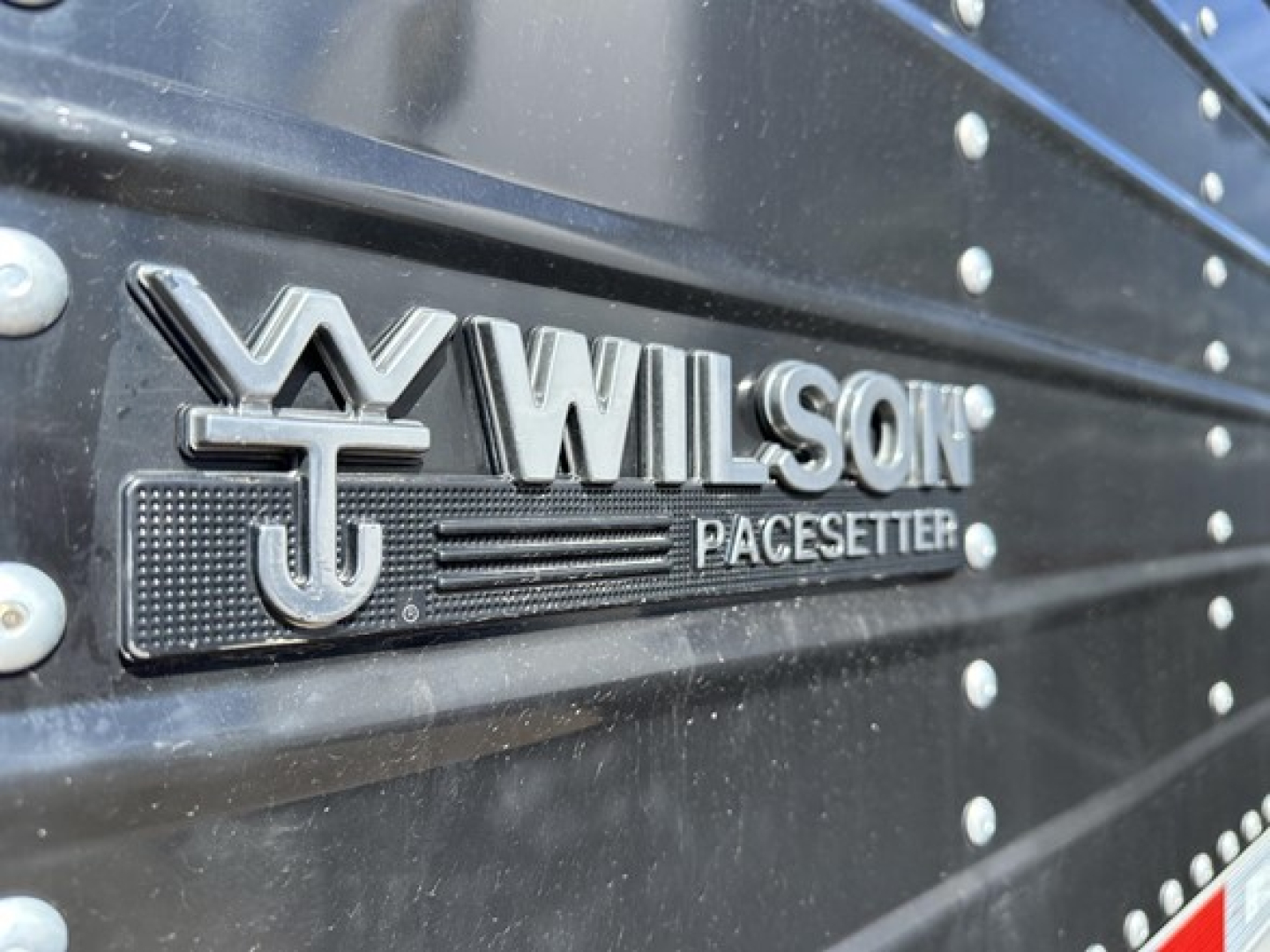 Wilson Pacese...  logo on black trailer side showing WILSON PACESITTER? text. The image shows a close-up of a Wilson logo on a black trailer with riveted steel panels.