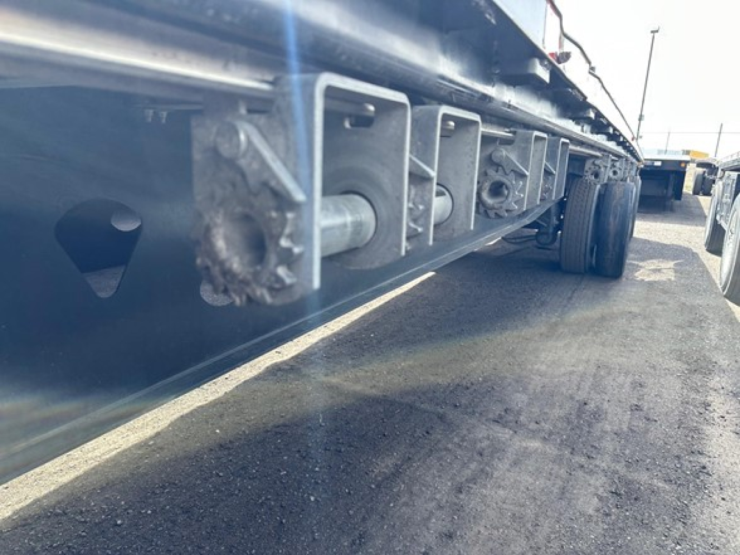 Trailer side underside showing frame rails and attachment brackets of a Manac 48' spread air steel flatbed, parked in lot.
