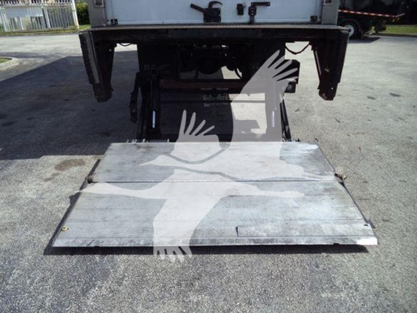 Flatbed/rear view of a refrigerated Mack MD6 truck with lift platform extended, showing metal ramp/platform and undercarriage components.