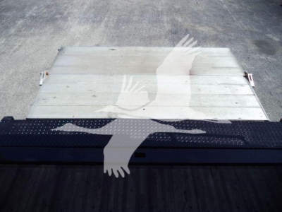 Flatbed truck bed with a metallic silver aluminum surface and a black perforated step looking at the rear of a Hino 195 cab; no legible text visible.