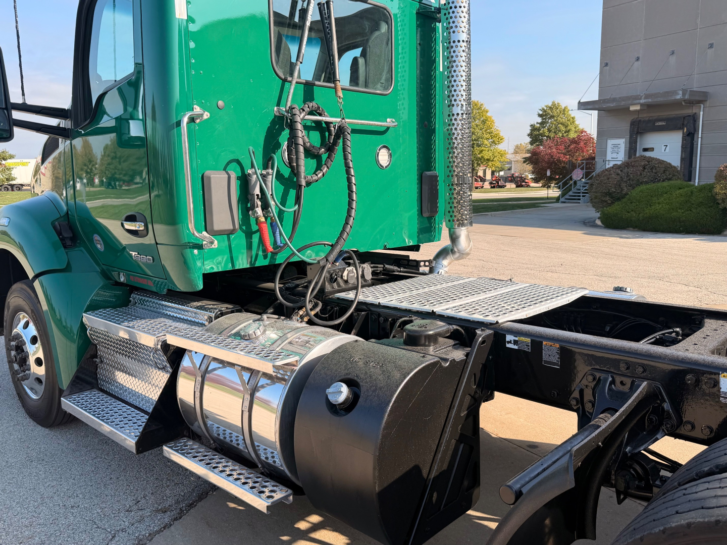 Kenworth T880 truck cab and fuel tank side view showing chrome steps and hoses with green cab and black chassis.