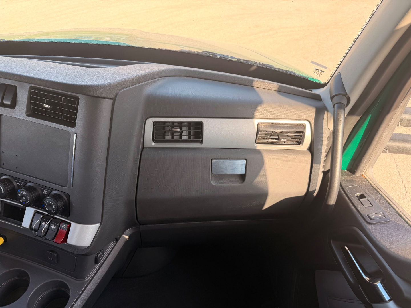 Kenworth T880 dashboard view showing steering wheel, center console with controls, air vents, passenger-side dash panel and window.