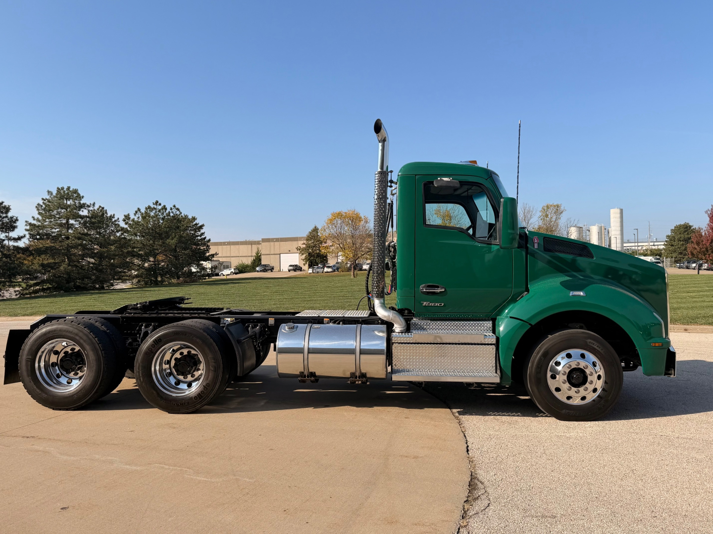 Kenworth T880 daycab tractor in green, side profile showing fuel tanks, exhaust stack, and dual rear axles.
