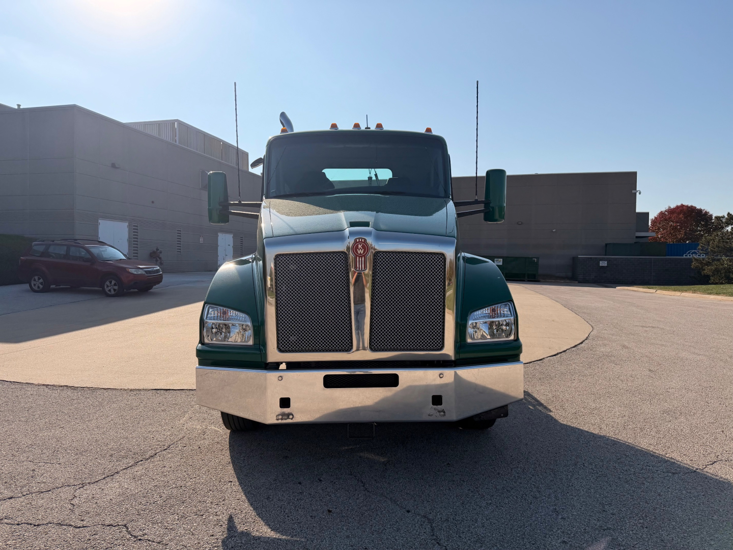 Kenworth T880 conventional daycab front view showing chrome grille, green body, large bumper; truck in parking lot.