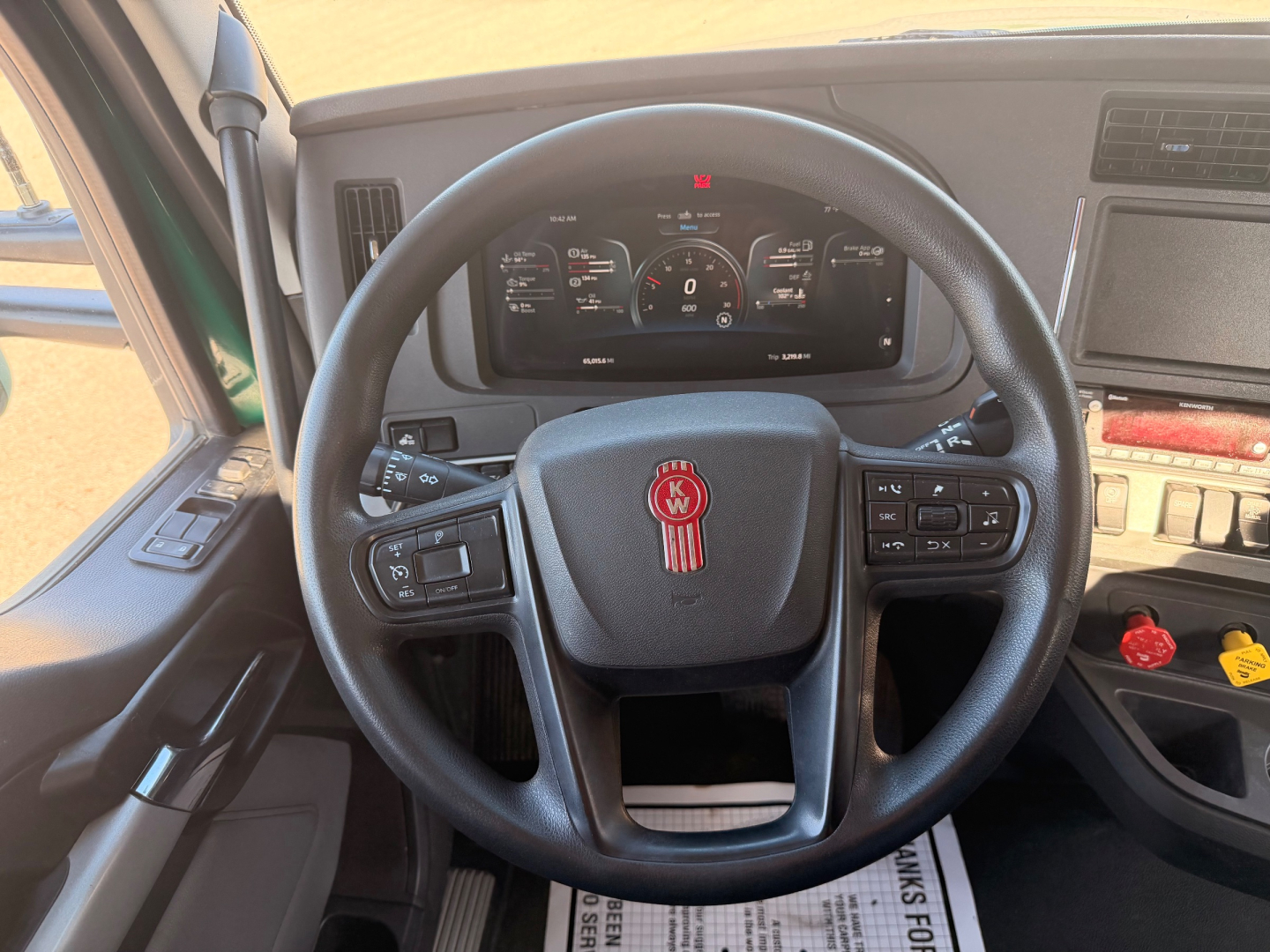 Kenworth T880 truck cabin steering wheel with instrument cluster visible, dashboard controls on right, steering wheel center emblem, and various gauges.