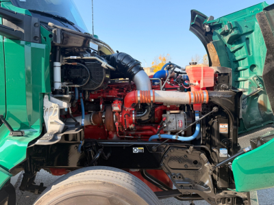 Kenworth T880 engine bay showing red engine block, various hoses, blue coolant line, black radiator hose, and green truck body with open hood