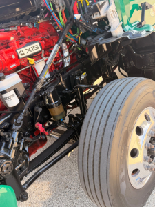 Kenworth T880 engine bay with red 6-cylinder  AXIS badging visible and front wheel with dual tires.