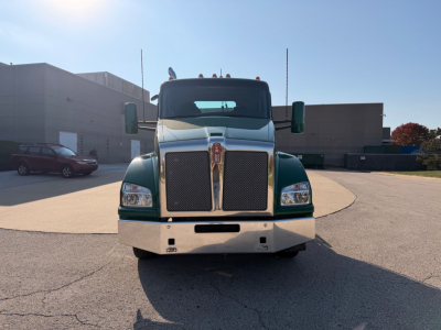 Kenworth T880 conventional daycab front view showing chrome grille, green body, large bumper; truck in parking lot.