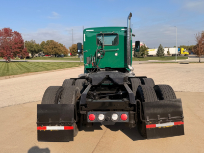 Kenworth T880 rear view showing dual rear axle configuration and green sleeper cab, with black mud flaps and rear lights.