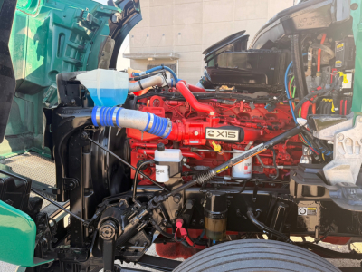 Kenworth T880 engine bay with red X15 engine and visible blue hoses, coolant reservoir, and various hoses and wiring in engine compartment.