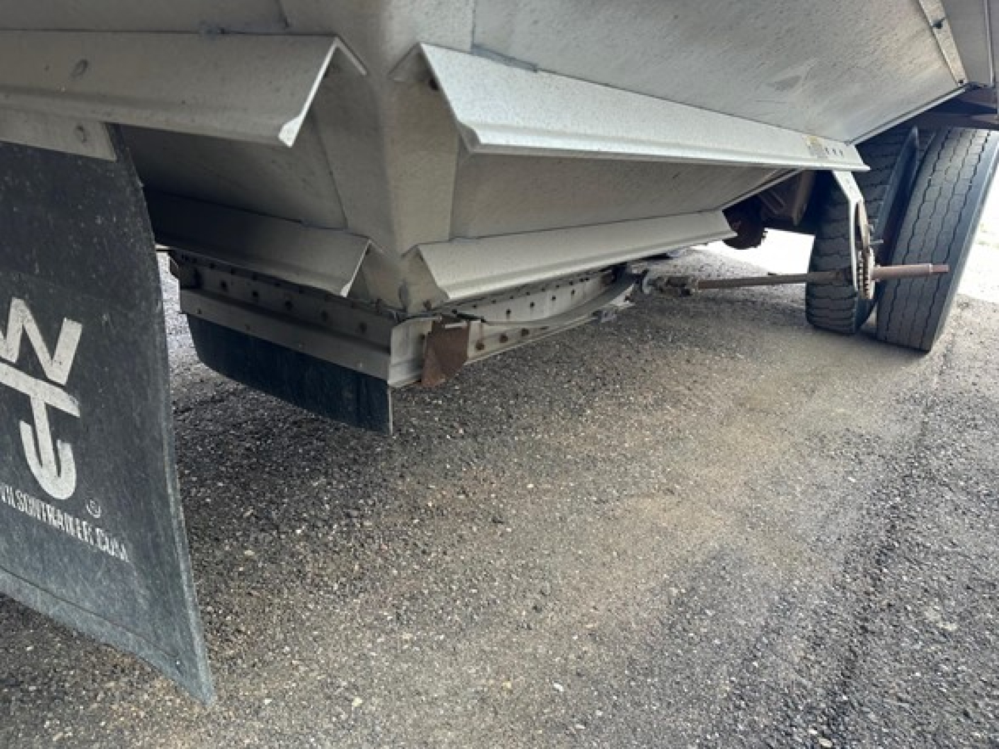 Trailer rear undercarriage showing underside of hopper grain trailer with dual wheels and mudflap.