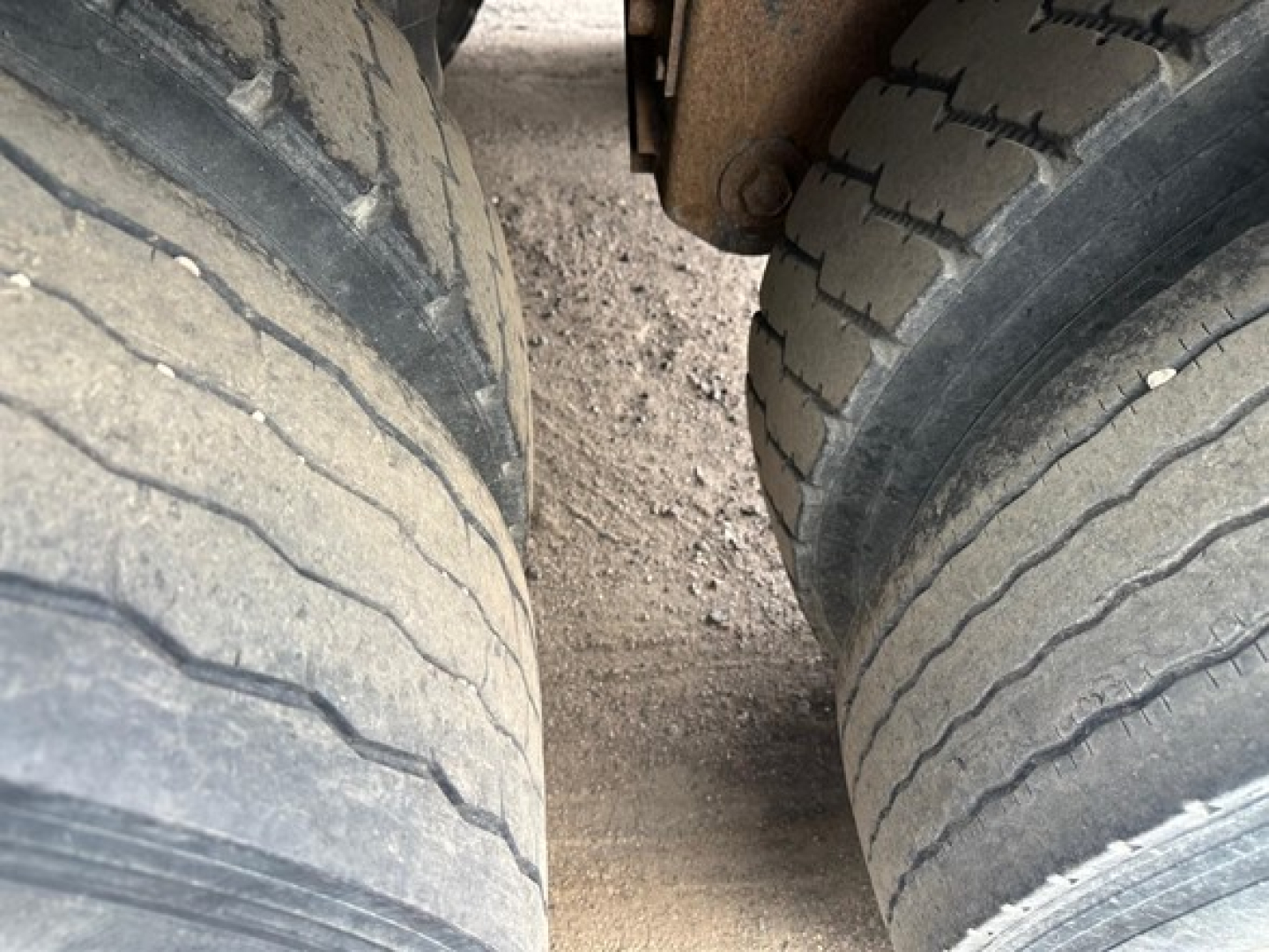 Trailer axle/wheels close-up showing dual-tire setup on Wilson grain trailer wheel hubs and grime on the dirt ground.