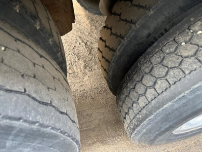 Trailer axle and tires of a Wilson grain trailer showing dual rear tires and treads; gravel ground beneath.
