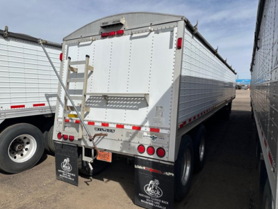 Rear view of a white Wilson grain trailer with dual rear doors, taillights, bumper, and mud flaps. VIN sticker and tires visible.