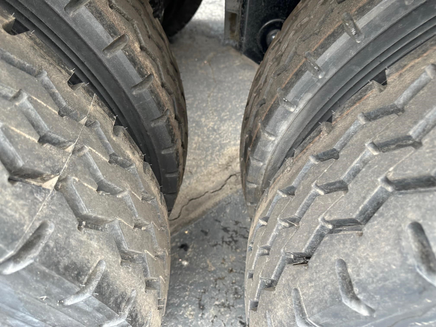 Dual rear tires of a trailer with tread pattern visible; close-up view undercarriage shows tire sidewalls and road grime.