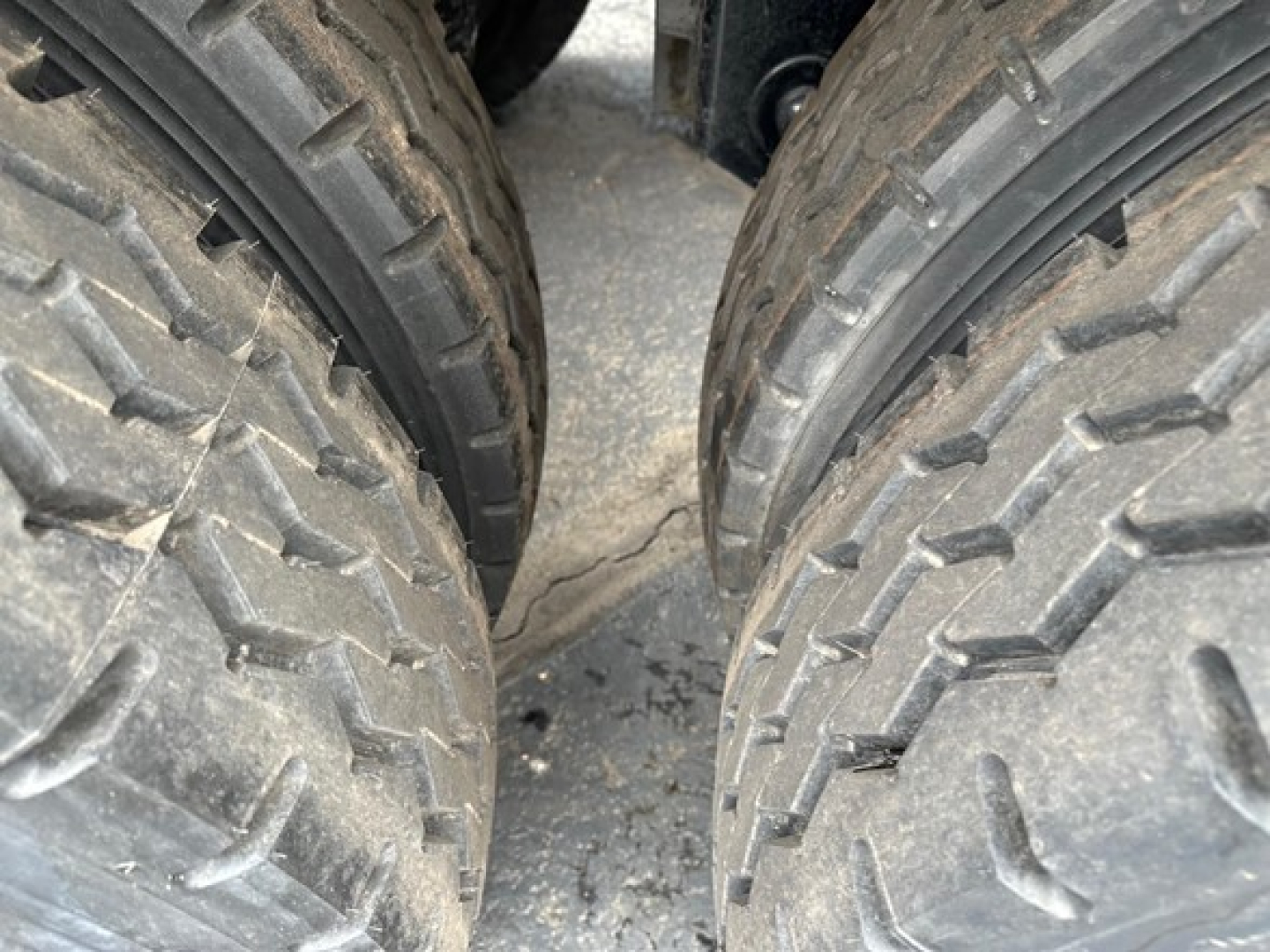 Dual rear wheels of a dump trailer with treaded tires; close-up view showing the wheel hubs and gaps between tires.