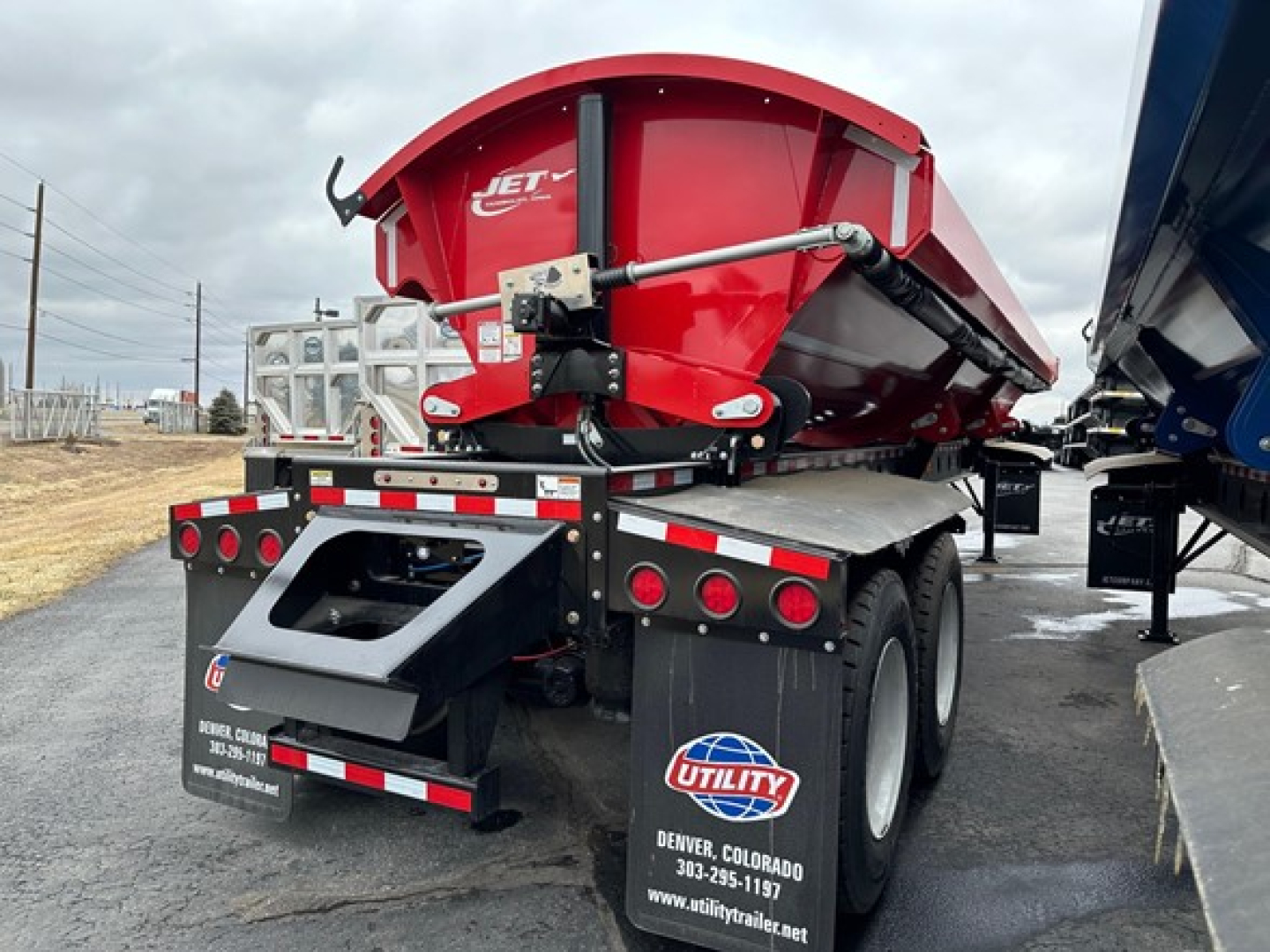 Jet side dump trailer in red, back view showing aerodynamic hopper and hydraulic mechanism, tail lights, and utility decals on mudflaps.