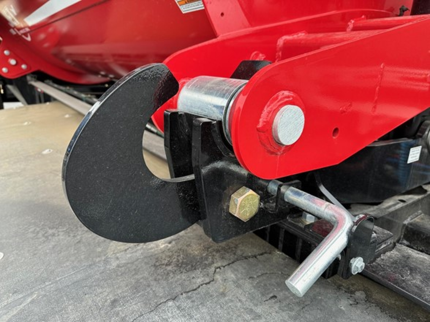 Trailer hitch coupler and red dump trailer frame showing a black adjustable hitch with bolt and metal pin near the curved shroud.