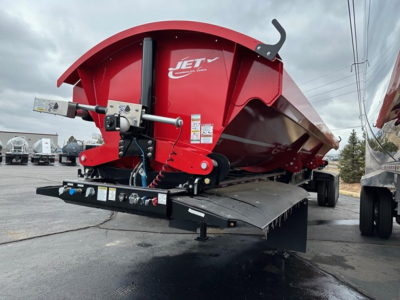Jet side dump trailer showing red JET hopper and hydraulic lift with controls on a black frame and ramp.