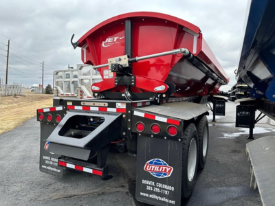 Jet Side Dump trailer in red color mounted on a black chassis showing its rear with lights and mud flaps, Utility trailer branding, and chrome hydraulic mechanism.
